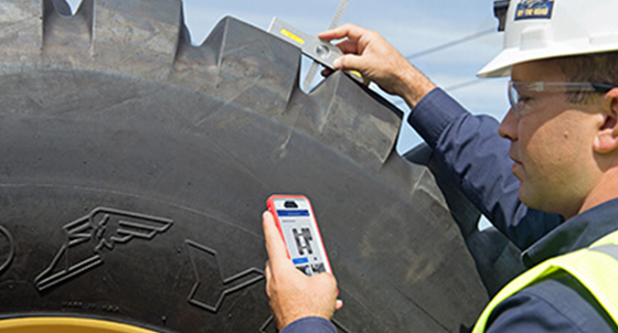 construction field worker measuring the tread depth of an OTR tire