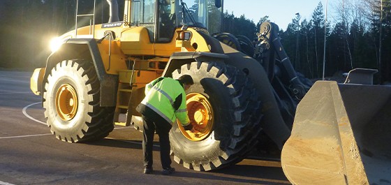 trabalhador de campo inspecionando um pneu off-road de estrada em uma retroescavadeira