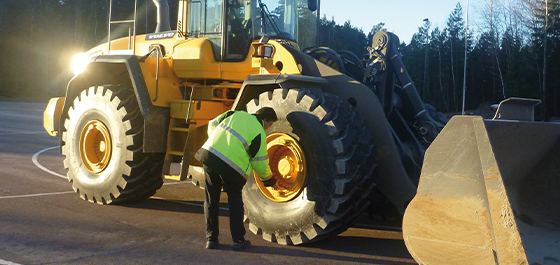 Arbeiter vor Ort, der einen Offroad-Reifen an einem Baggerlader inspiziert